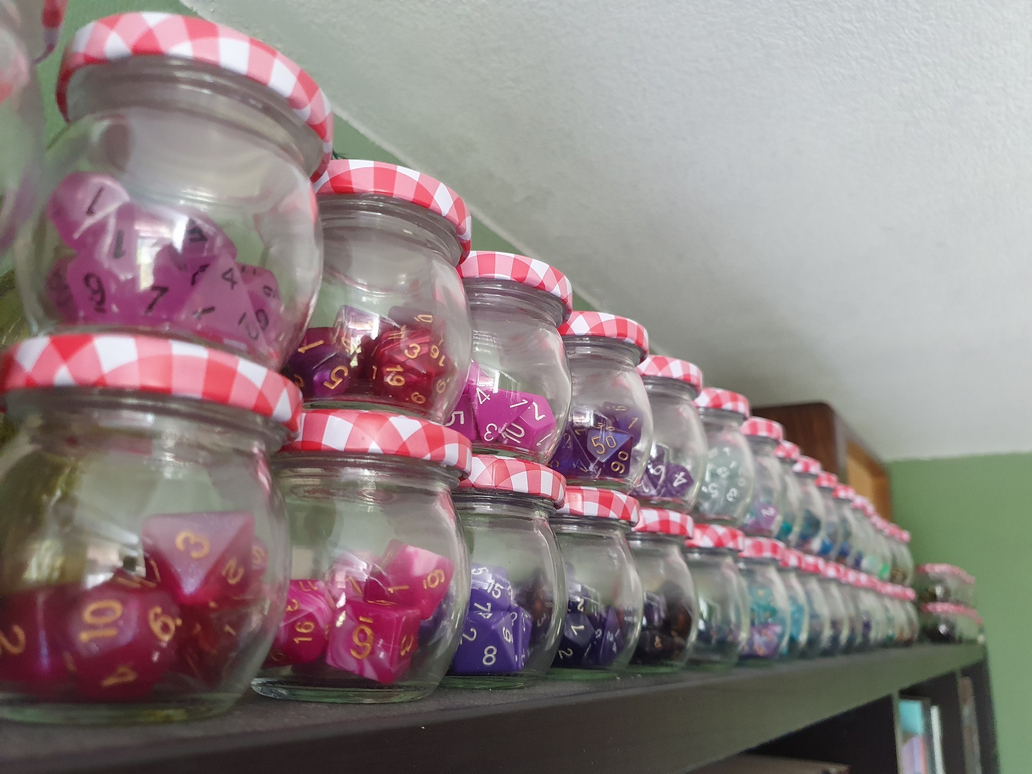 a closeup of a row of jars filled with dice. The first ones are pink, the other you can see are purple, blue, and green.