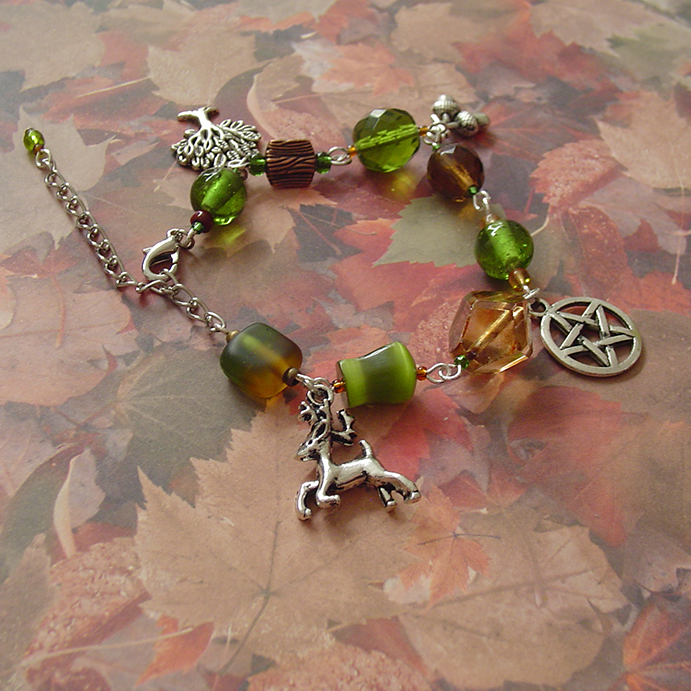 A beaded bracelet with green and brown beads in different shapes. Four charms hang from it: a stag, a pentagram, acorns, and a tree
