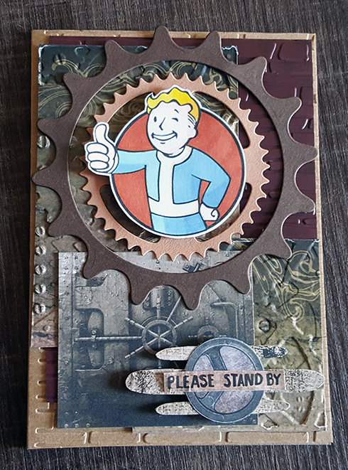 A card in browns and greys with various vault and gears. In the center is a stamped and coloured image of Vault Boy, from Fall Out.