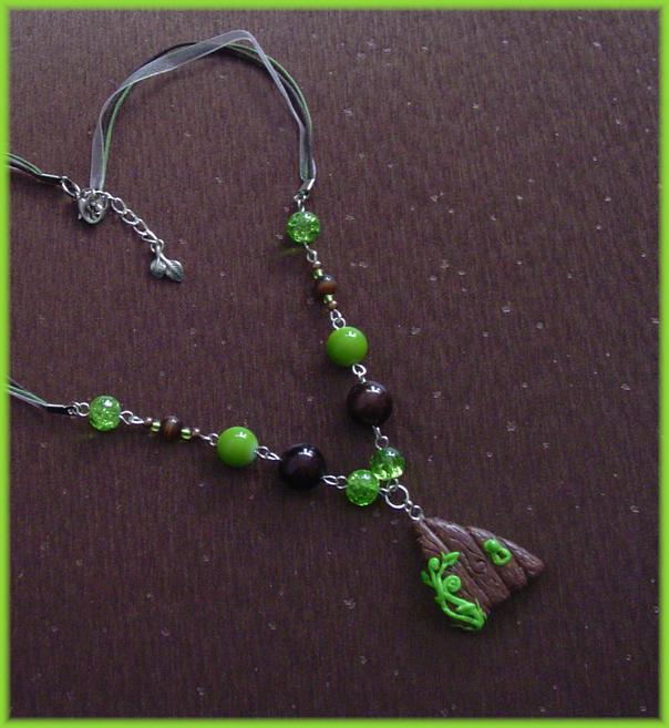 A beaded necklace with brown and green beads. The pendant is a small dark wooden faerie door, with swirling green vines on it. A small leaf charm hangs from the clasp in the back.