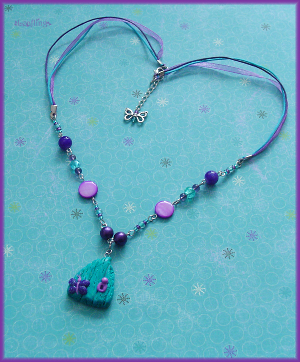 A beaded necklace with purple and turquoise beads. The pendant is a small turquoise faerie door, with a purple butterfly on it. A small butterfly charm hangs from the clasp in the back.