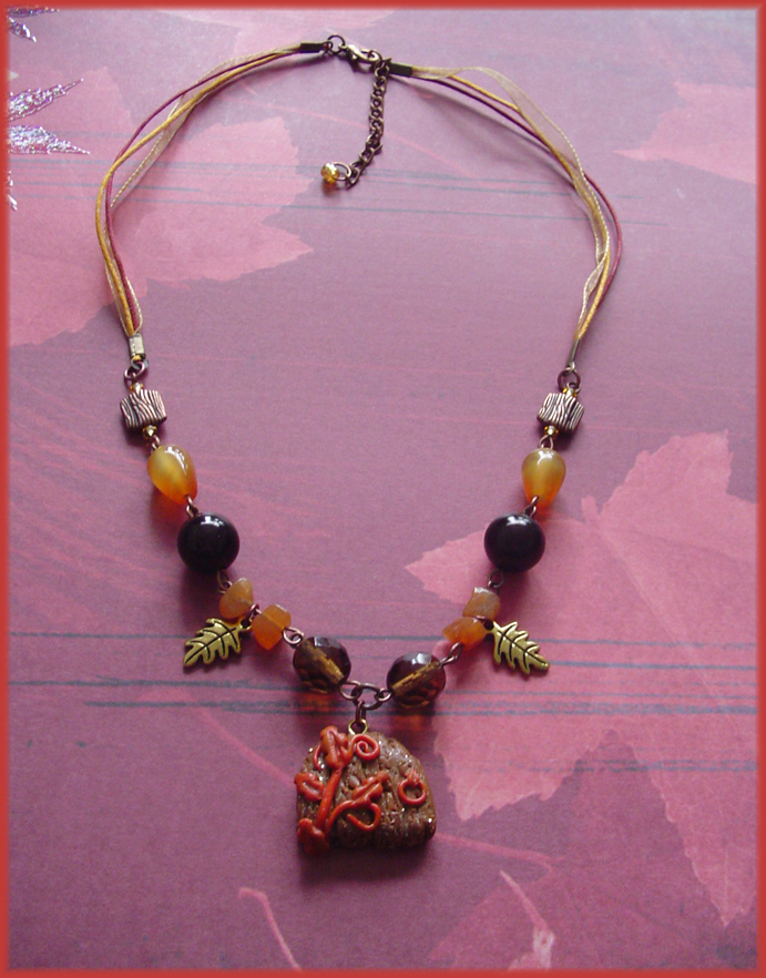 A beaded necklace in oranges and browns, with a small fairy door pendant. On the door are orange leaves and vines.