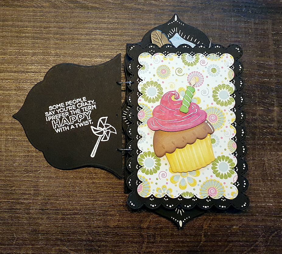 the second and third card of a set of birthday cards, which are bound together like a booklet. The left card is black, the text is white and reads: some people say you're crazy, I prefer happy with a twist! A small stamp of a pinwheel is next to it. The right card has a colourful patterned background, with a die-cut cupcake with bright pink frosting.