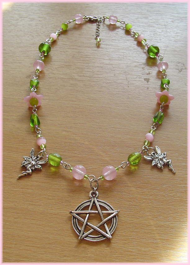 A beaded necklace with green and pink beads in various shapes and sizes. The centre pendant is a pentacle. Two smaller faerie charms hang on both sides.