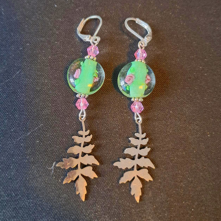 A set of earrings with silver fern pendants. Above are beads of soft green with painted pink roses on them.