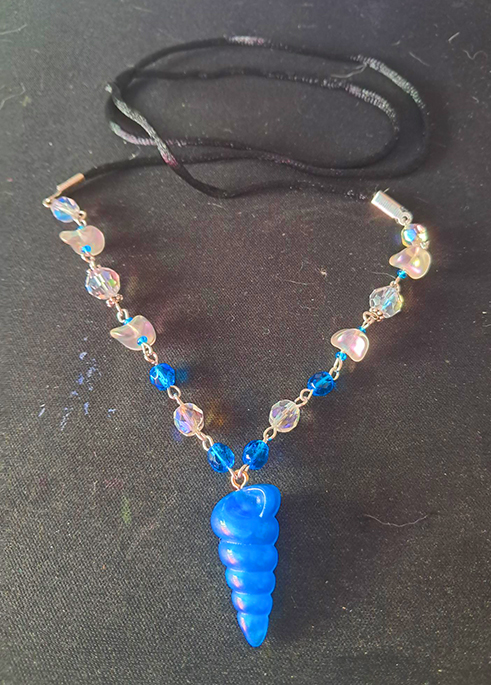 A beaded necklace with blue and iridescent white beads. The pendant is made from blue resin, and looks like a shell.