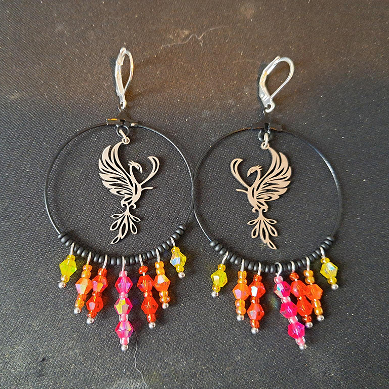 a pair of round ring earrings with a phoenix in the center. From the bottom dangle beads in reds, oranges, yellows, and pinks.
