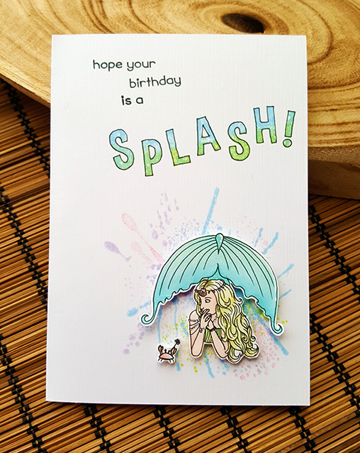 A white card with blues and greens splashed on it. In the bottom right is an image of a mermaid laying on her stomach, looking at her tiny crab friend. Text on the card reads: I hope your birthday is a SPLASH