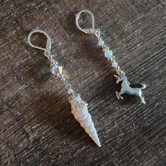 a set of mismatched earrings. Both have iridescent and silver beads. On one is a shell painted to look like a horn, on the other is a silver unicorn charm.