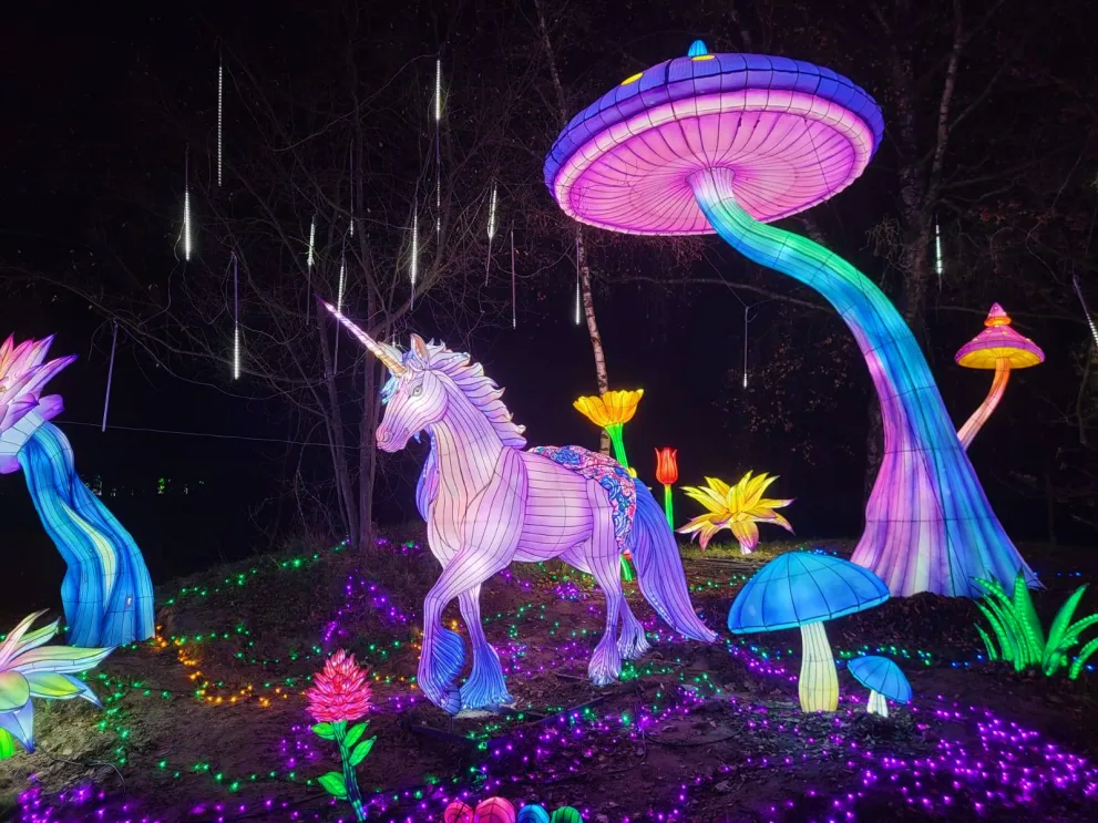 a photo of lit up sculptures of a unicorn, several flowers, and a tree